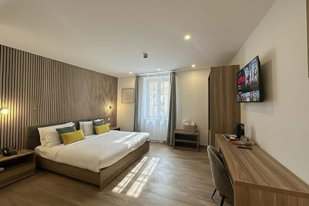 A modern hotel room with a bed, bedside table, desk, and a TV mounted on the wall.