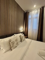 Une chambre d’hôtel avec un lit, une tête de lit, une table de chevet et une fenêtre avec des rideaux.