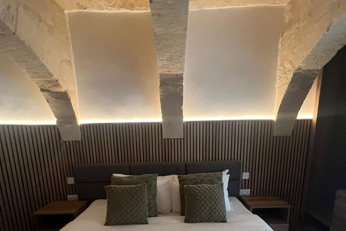 A hotel room with a large bed, a wooden headboard, and a stone wall.