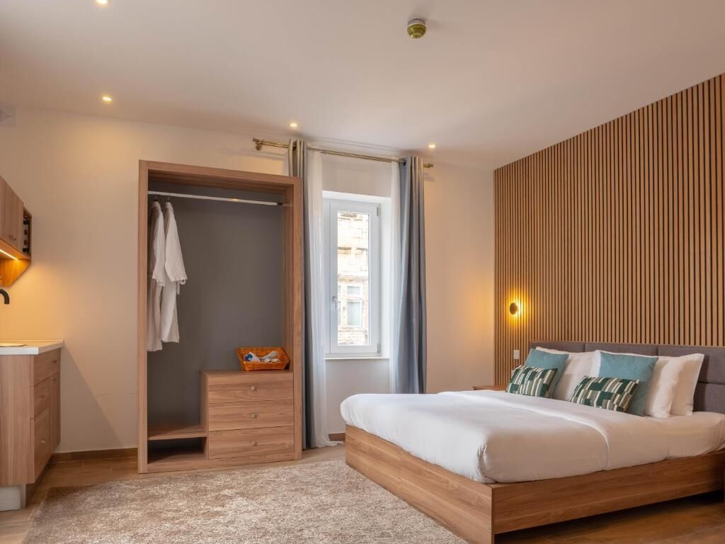A bedroom with a bed, a wardrobe, a bedside table, and a window.