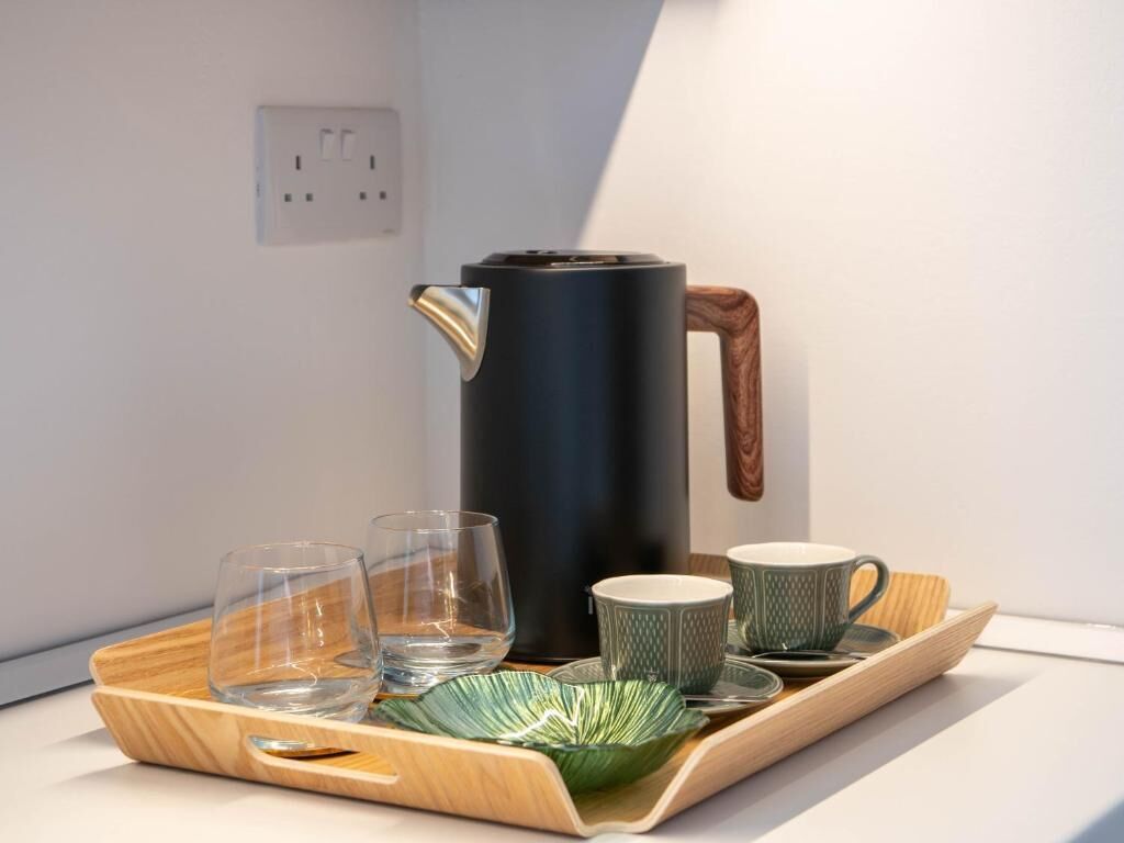 Una cocina moderna con un hervidor negro, dos vasos y una bandeja con un bol verde y tazas.