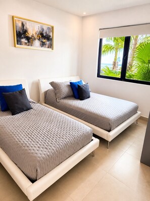 A modern bedroom with two beds, a painting on the wall, and a window with a view of palm trees. - Luxury 3BD W/Private Pool~Golf~Padel~Gym~Beach (Playa del Carmen)