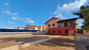 A courtyard with a paved area, a building with a red facade, and a blue structure in the background. - Savvy Studio Apt@RealShala Galaxy-School-Adjiringanor (Ashaley Botwe)