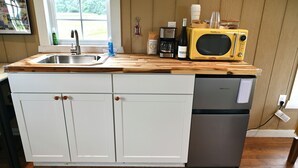 Eine Küche mit Holzarbeitsplatte, Spüle, Mikrowelle, Kaffeemaschine und Kühlschrank.