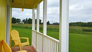 Eine Veranda mit zwei gelben Stühlen, einem Deckenventilator und Blick auf ein grünes Feld.