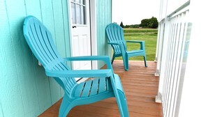 To turkis Adirondack-stole på en træterrasse med en hvid dør og udsigt til et grønt græsareal.