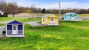 Tre små, etagers huse i forskellige farver og med enkel arkitektur, beliggende på en græsklædt skråning under en klar himmel.