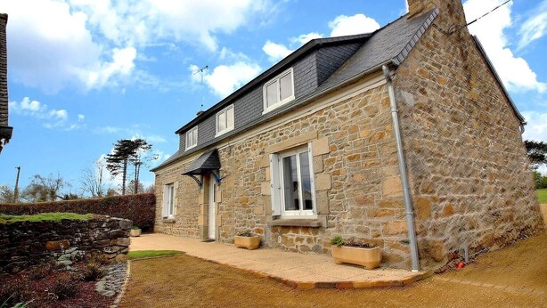 Une maison en pierre avec un toit en pente, un porche à l’avant et un petit jardin.