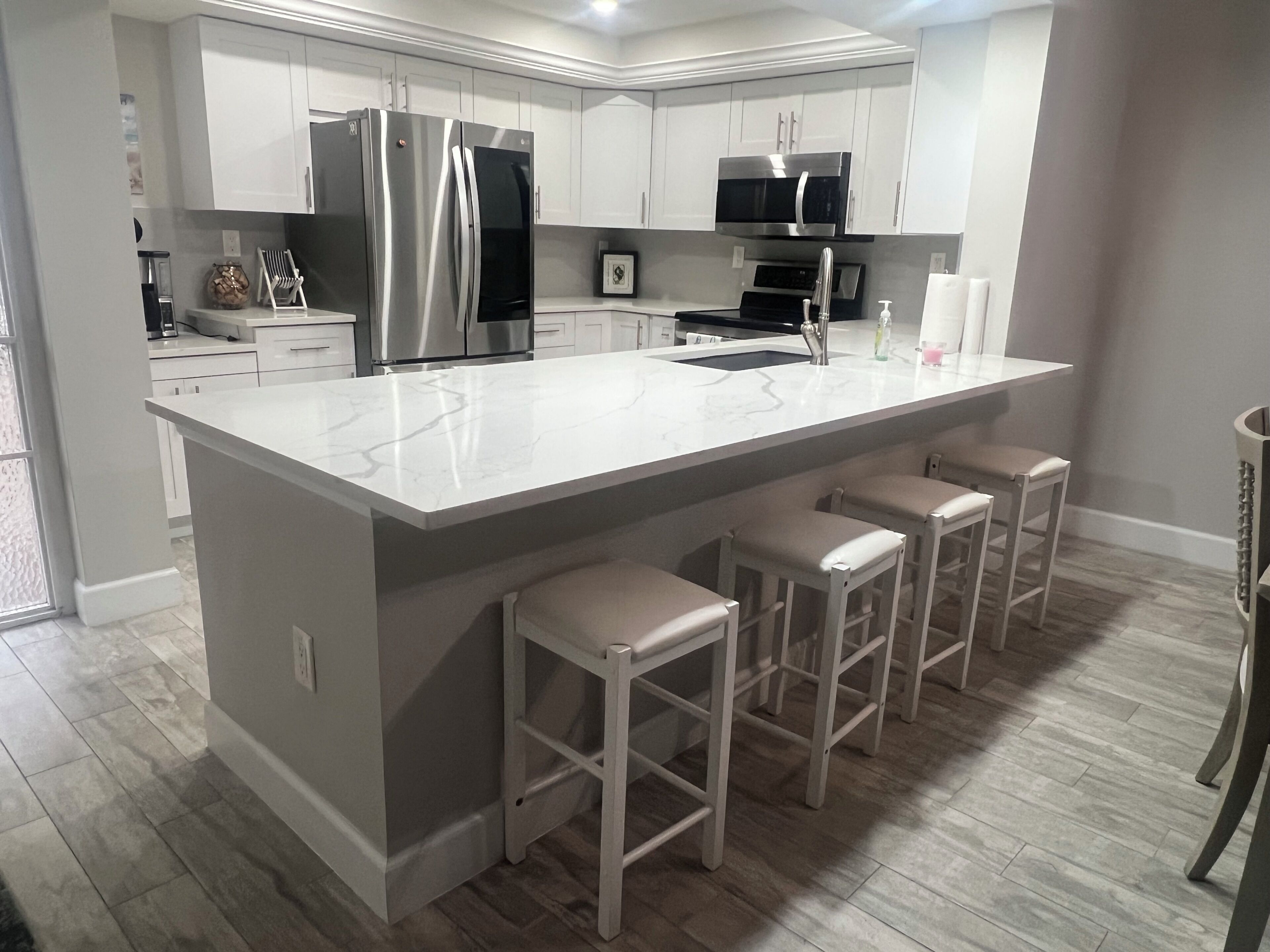 Uma cozinha moderna com armários brancos, eletrodomésticos de aço inoxidável, bancada de mármore e banquetas.