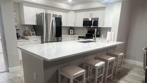 Una cucina moderna con mobili bianchi, elettrodomestici in acciaio inossidabile, un piano di lavoro in marmo e sgabelli da bar.