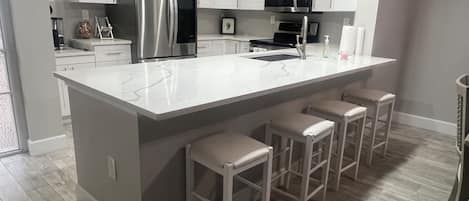 A modern kitchen with white cabinetry, stainless steel appliances, a marble countertop, and bar stools.
