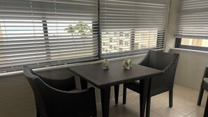 Un balcone con tavolo e sedie, vista su palme e pavimento piastrellato.