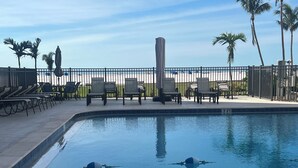 Una piscina con lettini e ombrelloni, circondata da una recinzione e palme.