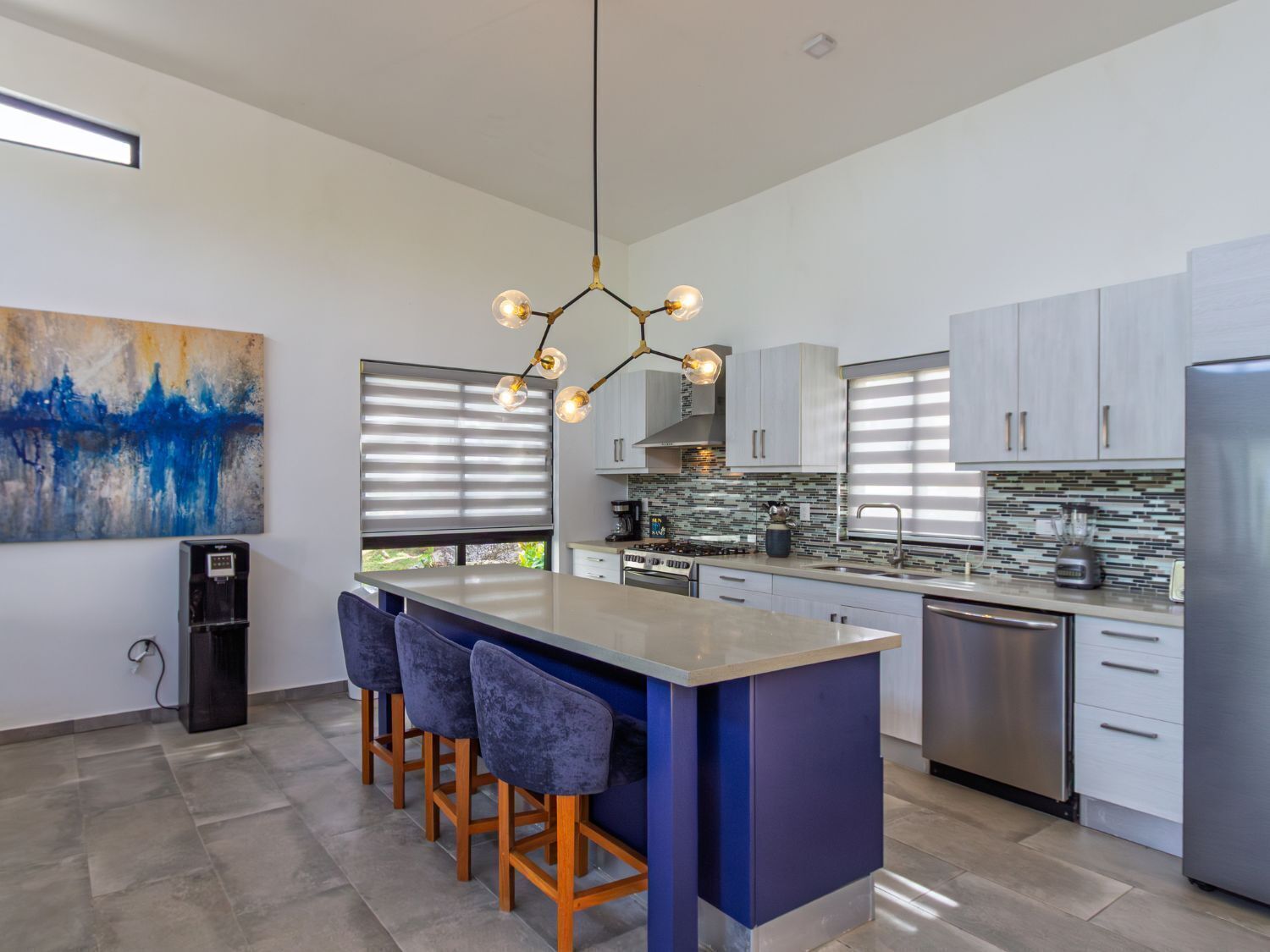 A modern kitchen with a central island, bar stools, stainless steel appliances, and a large abstract painting on the wall.