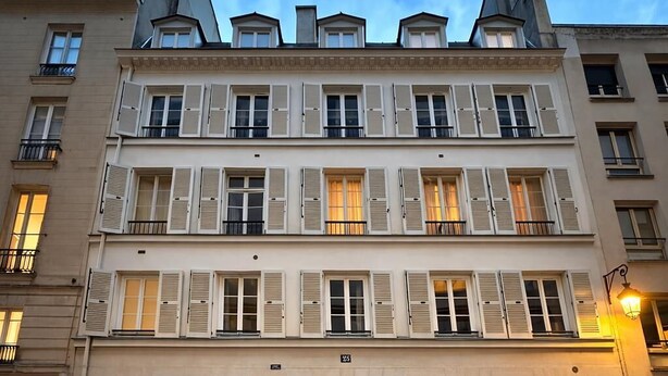 Ein mehrgeschossiges Gebäude mit einer symmetrischen Fassade, großen Zwerchgiebelüren und zahlreichen Fenstern mit Fensterläden.