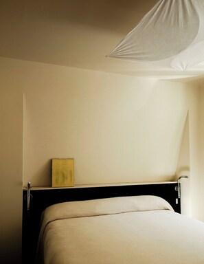 A minimalist hotel room with a bed, a bedside table, and a hanging light fixture. - Mont Thabor Vendôme Residence (Paris)