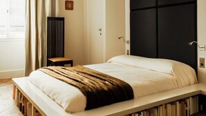 Ein Schlafzimmer mit einem Bett, Regalen unter dem Bett, einem Heizkörper, einem Fenster mit Vorhängen und einer Deckenleuchte.