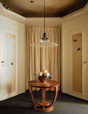 A room with a round wooden table, a hanging light fixture, and a curtain backdrop. - Mont Thabor Vendôme Residence (Paris)