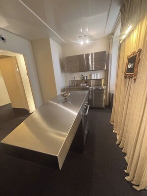 A modern kitchen with stainless steel appliances, a long countertop, and a dining area. - Mont Thabor Vendôme Residence (Paris)