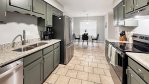 Una cocina moderna con encimeras de granito, electrodomésticos de acero inoxidable y un comedor con mesa y sillas.