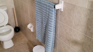 Une salle de bain équipée de toilettes, d’une ventouse, d’une poubelle et d’un porte-serviettes avec une serviette.