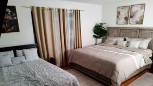 Une chambre avec deux lits, une tête de lit en bois, une plante en pot et un tableau accroché au mur.