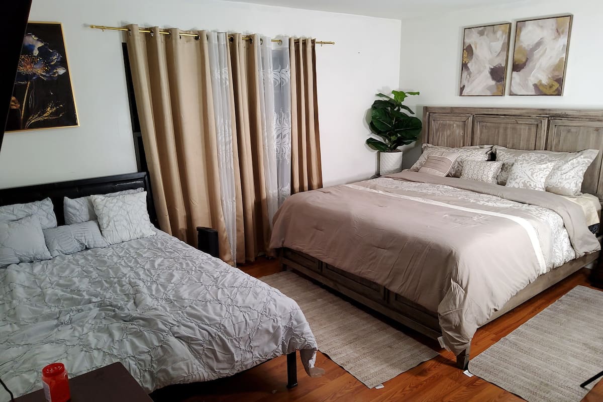 A bedroom with two beds, a wooden headboard, a potted plant, and a painting on the wall.