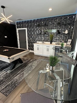 A modern kitchen with white cabinets, a black backsplash, and a dining area with a glass table and chairs. - 3 bedroom Townhome | Skyline Rooftop + Hot tub (Houston)