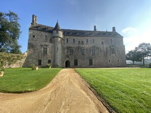 A large stone castle with a central entrance, surrounded by well-maintained lawns and a clear sky.