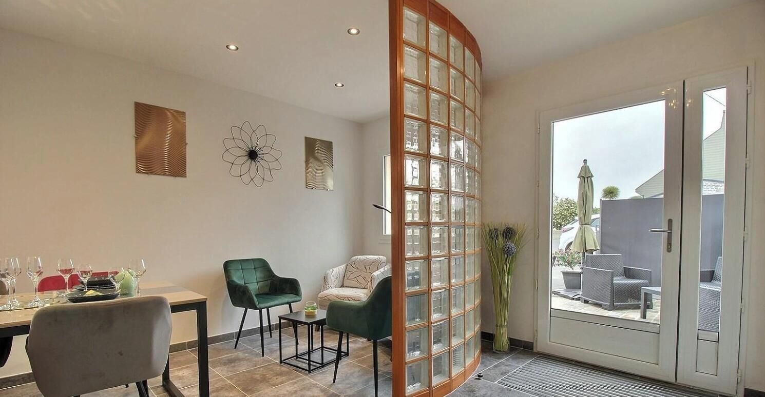 Ein Zimmer mit Esstisch für vier Personen, zwei Stühlen, einem kleinen Beistelltisch und einer großen Schiebetür zu einem Außenbereich mit Möbeln.