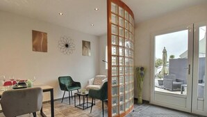 A room with a dining table set for four, two chairs, a small side table, and a large sliding glass door leading to an outdoor area with furniture. - Ty Bihan - PLEUMEUR GAUTIER (PLEUMEUR GAUTIER)