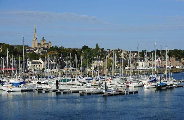 A marina with numerous boats docked, a prominent church with a tall spire in the background, and a town with buildings along the waterfront.
