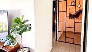 A hallway with a potted plant, a wooden desk, and a room with a sliding door and hanging lights. - Resort-Style Condo- Pool, Patio, Playground + Palapa Lounge (Aldea Hortus)