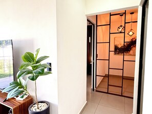 A hallway with a potted plant, a wooden desk, and a room with a sliding door and hanging lights. - Resort-Style Condo- Pool, Patio, Playground + Palapa Lounge (Aldea Hortus)