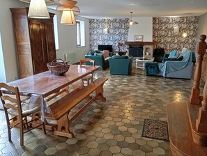 Un salon avec une table à manger en bois, des canapés bleus, une cheminée et un papier peint à motifs.