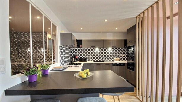 Une cuisine moderne dotée d’un îlot central, d’appareils électroménagers intégrés et d’un revêtement mural décoratif.
