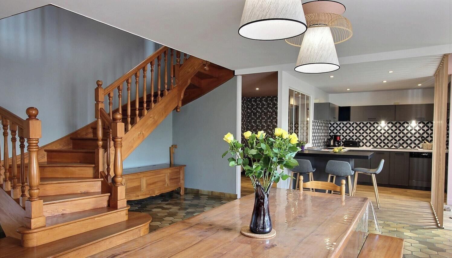 A staircase with wooden balusters, a dining area with a table and chairs, and a kitchen with a patterned backsplash.