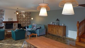 Un salon avec une cheminée, un canapé, une table à manger et deux lampes suspendues.