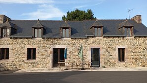 Un bâtiment en pierre doté de nombreuses fenêtres et d’une porte, une table de pique-nique et un ciel dégagé.