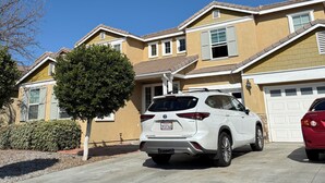 A residential building with a garage, a white SUV parked in the driveway, and a tree in front.