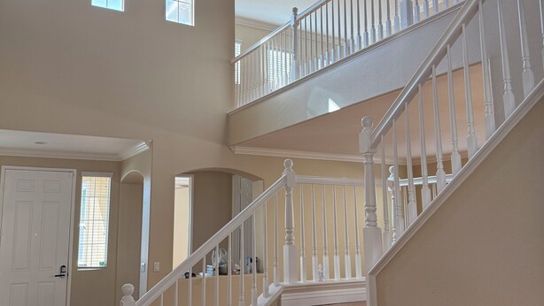 A multi-level wooden staircase with white railings, a beige interior, and a view of the upper floor.