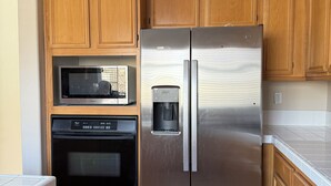 A kitchen with wooden cabinets, a stainless steel refrigerator, a microwave, and an oven.