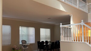 A spacious living area with a dining table, chairs, a high ceiling, and a staircase.