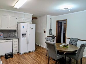 Une cuisine avec des meubles blancs, un réfrigérateur, une table à manger avec quatre chaises et un plancher en bois.