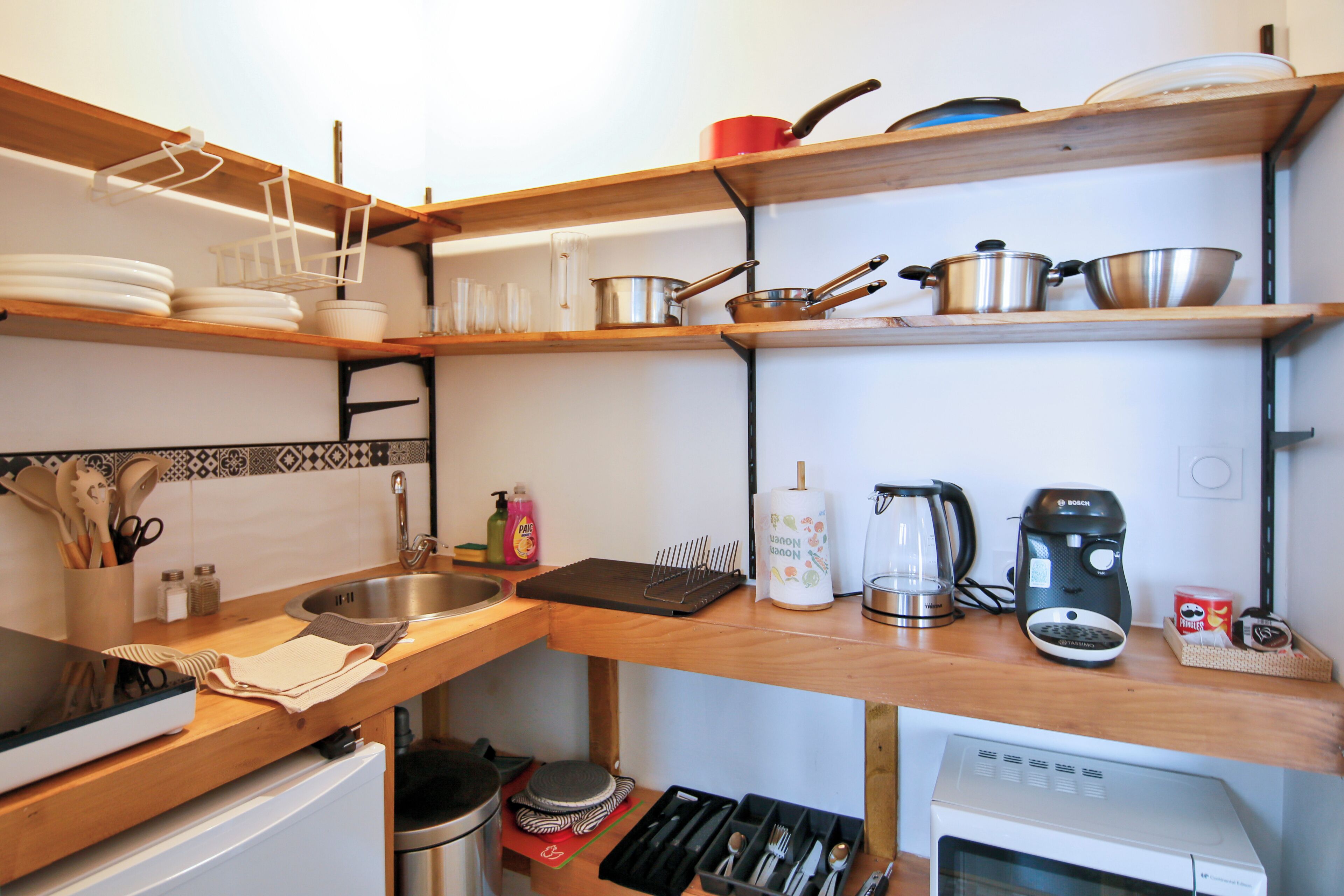 A kitchen with wooden shelves, a sink, a coffee maker, and various kitchen utensils.