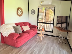 Un sofá rojo con cojines, una mesita redonda con un florero y un televisor sobre un mueble bajo.