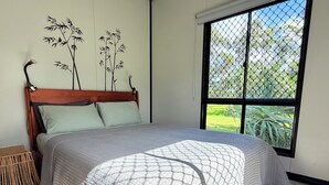 Ein Schlafzimmer mit Bett, einem Holzkopfteil, einem Fenster mit Blick auf Grünflächen und einer Wand mit Bambusdekoration.
