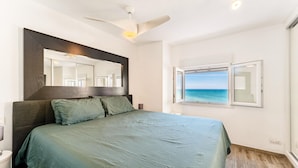Ein Schlafzimmer mit Bett, Deckenventilator, Fenster mit Meerblick und Spiegel über dem Bett.