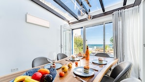Ein Essbereich mit Blick auf das Meer, ein Tisch gedeckt mit Tellern, Gläsern und einer Obstschale.