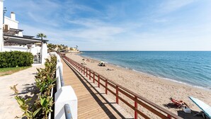 Uma passarela costeira que leva a uma praia com um deck de madeira e guarda-corpos vermelhos.